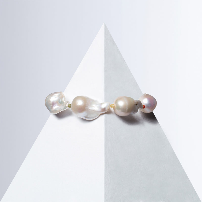 Ostro - I baroque pearl bracelet with small colorful gemstones between the pearls on a white pyramid