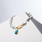 Scarab charm hanging from the HoS Lock of a baroque pearl necklace on a white block