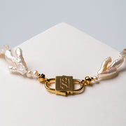 Close-up of the gold-tone HoS Lock on Sui Generis between branch-shaped and round pearls