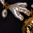 Close-up of Sui Generis branch-shaped pearls and gold-tone ornaments beside part of the HoS Mask
