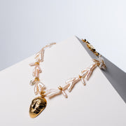 Sui Generis freshwater pearl necklace with gold-tone HoS Mask pendant and HoS Lock on a white block